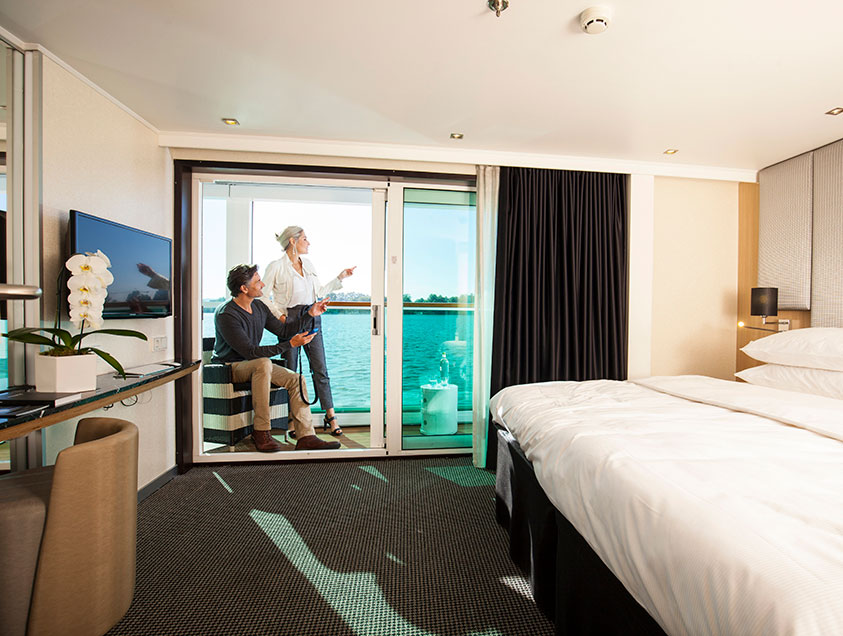 A man and woman looking out to the river from their Scenic Sun Lounge in the Junior Balcony Suite