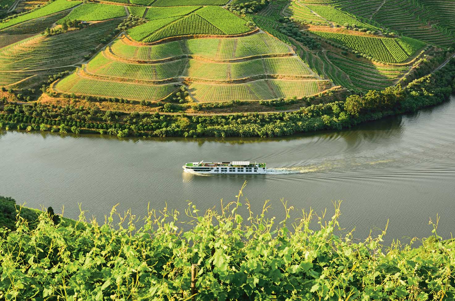 River cruise ship sailing around the bend of a river surrounded by wineries
